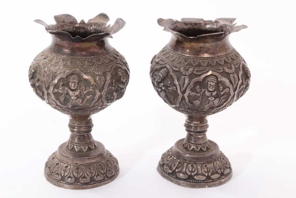 Lot 251 - Pair late 19th/early 20th century Indian white metal pedestal vases, with embossed decoration of Hindu gods and flared petal style rims on circular domed bases. Possibly Madras. All at approximatel...