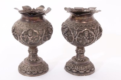 Lot 251 - Pair late 19th/early 20th century Indian white metal pedestal vases, with embossed decoration of Hindu gods and flared petal style rims on circular domed bases. Possibly Madras. All at approximatel...
