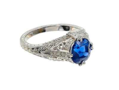 Lot 487 - A fine sapphire single stone ring with a natural cushion cut blue sapphire weighing 2.66ct in four claw setting with pavé set diamonds to the claws and bezel, pierced decoration on engraved shank....