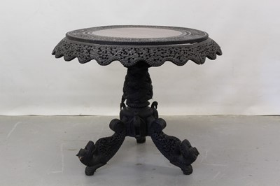 Lot 1264 - 19th century Burmese carved and ebonised hardwood centre table with ornate bird, animal, and temple decoration on animal head terminals, 92cm diameter.