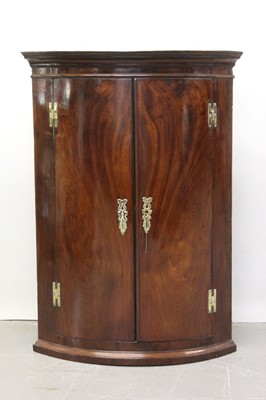 Lot 1309 - George III mahogany bowfront hanging corner cupboard with two doors enclosing painted shelves 103 cm high, 73 cm wide.