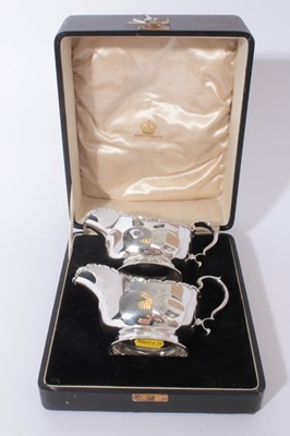 Lot 323 - Pair of George V silver sauce boats of helmet form with faceted decoration and scroll handles, raised on oval pedestal feet, in fitted case, (Birmingham 1934)