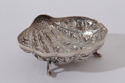 Lot 220 - Late 19th / early 20th century Burmese silver dish of shell form, with embossed decoration, raised on three feet modelled as coiled fish, (Unmarked) All at approximately 2.5oz 10.5cm in diameter.