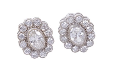 Lot 460 - Pair of diamond cluster earrings, each oval flower head cluster with a central oval cut diamond surrounded by a border of round brilliant cut diamonds in millegrain setting. Estimated total diamond...