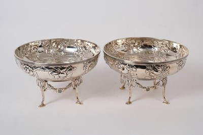 Lot 348 - Pair of Edwardian silver dishes of circular form with embossed wrythen floral decoration below reeded borders, raised on separate stands with reeded and foliate swag decoration, on four hoof feet,...