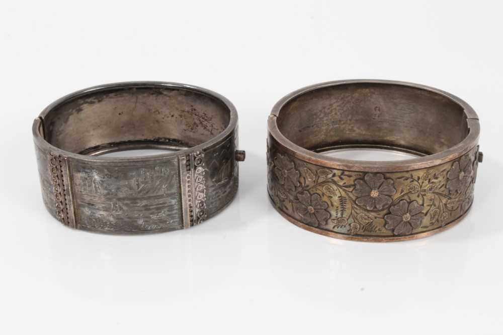 Lot 20 - Two Victorian silver hinged bangles, one with applied and textured floral design, Birmingham 1883, the other with engraved scenes depicting various boats in coastal bays