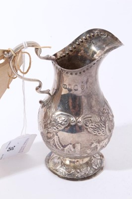 Lot 36 - George III Irish silver cream jug with repousse cattle in landscape panels, scroll handle and circular pedestal foot (Dublin 1792), together with a George IV Irish silver cream ladle (Dublin 1826),...