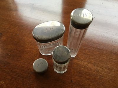Lot 247 - Three George V silver topped glass toiletry jars, together with another lid, each engraved JB (London 1912)