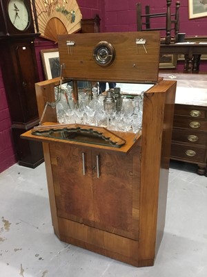 Lot 850 - Art Deco figured and cross-banded walnut veneered cocktail cabinet with cantilever mechanism opening to reveal the fitted mirrored interior with cut glasses, and cupboard below enclosed by two door...