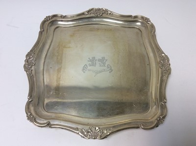 Lot 234 - George V silver salver of square form with double engraved armorial and motto, and scroll and acanthus leaf border, raised on four scroll feet