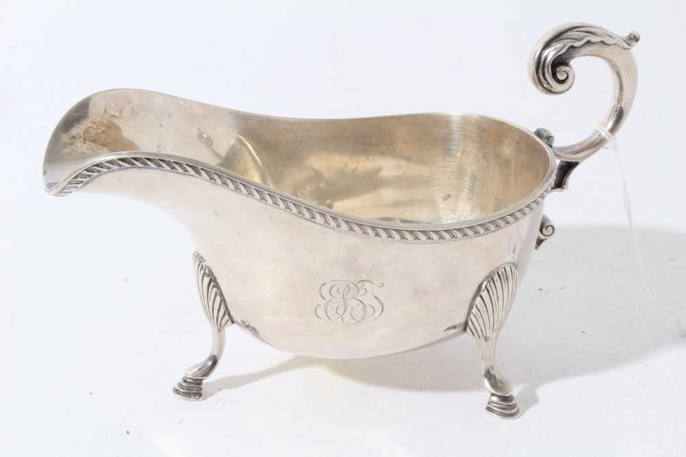 Lot 44 - George V silver sauce boat of helmet form with gadrooned borders and scroll handle, raised on three hoof feet, retailed by Tiffany & Co (London 1934)