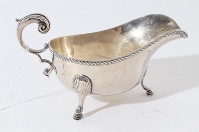 Lot 44 - George V silver sauce boat of helmet form with gadrooned borders and scroll handle, raised on three hoof feet, retailed by Tiffany & Co (London 1934)
