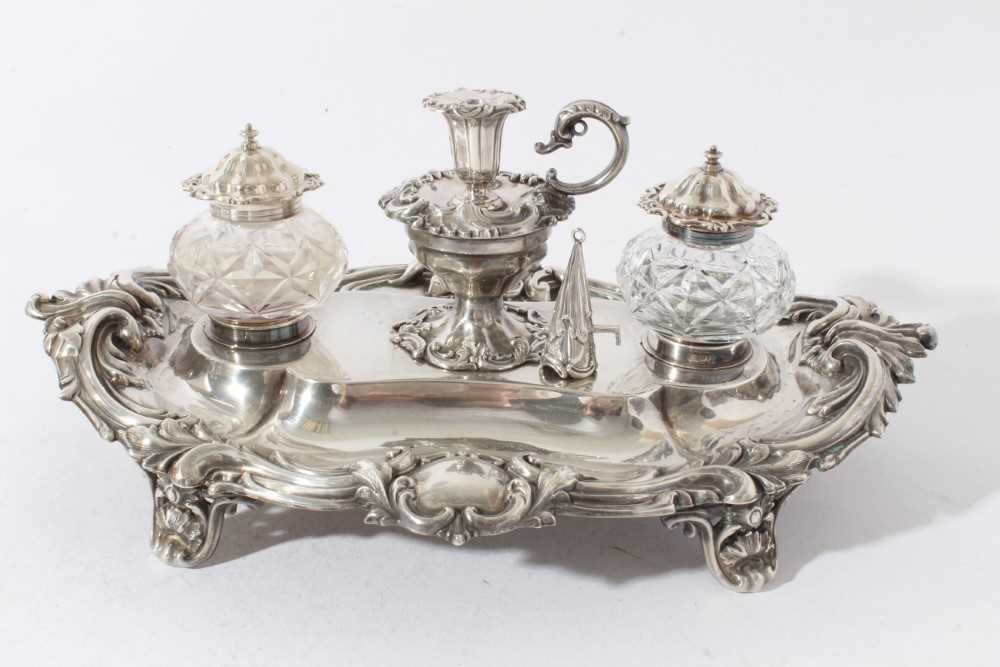 Lot 157 - Victorian silver inkstand of oval form, with shell, scroll and leaf border, central chamberstick with snuffer and a pair of cut glass inkwells with silver mounts, on four scroll feet (London 1891)