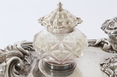 Lot 157 - Victorian silver inkstand of oval form, with shell, scroll and leaf border, central chamberstick with snuffer and a pair of cut glass inkwells with silver mounts, on four scroll feet (London 1891)