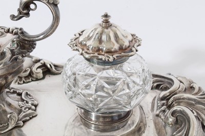 Lot 157 - Victorian silver inkstand of oval form, with shell, scroll and leaf border, central chamberstick with snuffer and a pair of cut glass inkwells with silver mounts, on four scroll feet (London 1891)