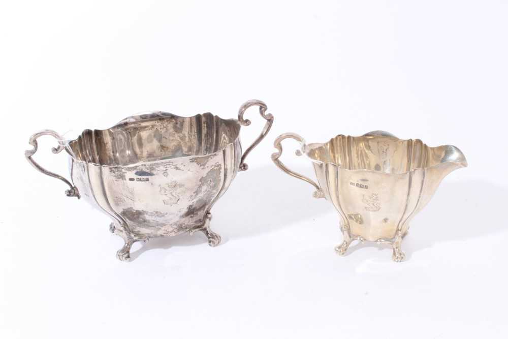 Lot 109 - Edwardian silver two handled sugar bowl with fluted decoration, engraved armorial and scroll handles, raised on four scroll feet, together with a matching milk jug, (Sheffield 1906)