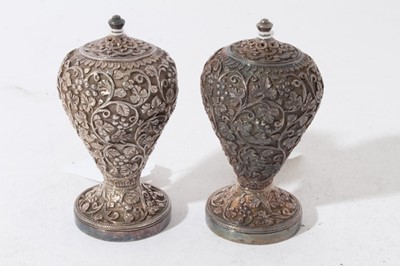 Lot 140 - Pair of good quality late 19th century Indian white metal pepperettes of ovoid form with ornate vine leaf decoration in relief, on circular feet with screw in covers to bases