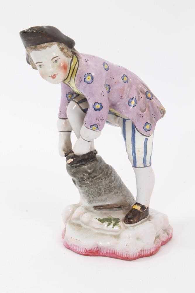 Lot 102 - 19th century French faience figure of a boy tying his shoelaces, wearing tricorn hat, lilac floral jacket, yellow shirt, and blue and white striped breeches, mark on the base for Theodore Deck, 16....