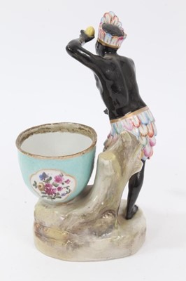 Lot 98 - Late 19th century Dresden figural porcelain sweetmeat, emblematic of Africa, the male figure shown wearing feather headdress and skirt, holding a lemon, the bowl painted with panels of flowers and...