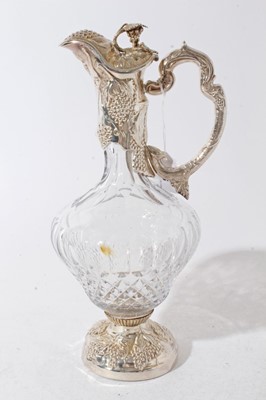 Lot 205 - Victorian style cut glass claret jug of bulbous form, with facet cut decoration, silver mount with embossed fruiting vine decoration, and hinged cover, with integral handle, silver foot of circular...