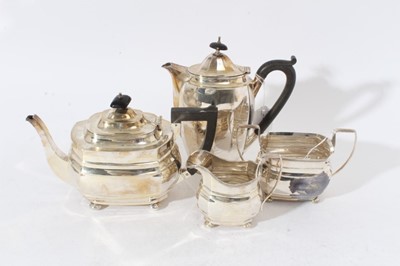 Lot 221 - George V silver three piece teaset comprising teapot of cauldron form with faceted decoration, with engraved armorial, domed hinged cover with ebony finial and angular ebony handle, on four bun fee...