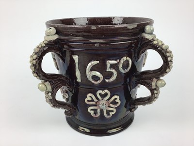 Lot 77 - Castle Hedingham pottery four handled loving cup with applied 1650 and floral decoration on brown ground, 18cm high