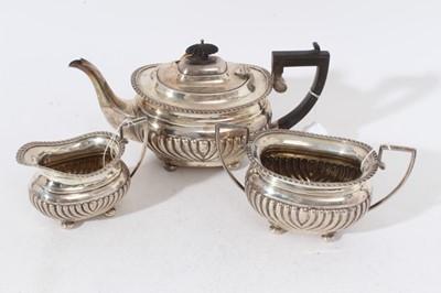 Lot 246 - Edwardian silver three piece teaset comprising teapot of cauldron form with fluted decoration, gadrooned border, domed hinged cover with ebony finial and angular ebony handle, on four bun feet, tog...
