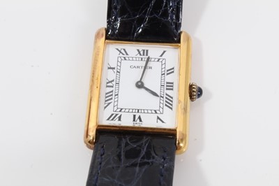 Lot 311 - Cartier Tank wristwatch, the white rectangular dial with black enamel Roman numerals and black hands, quartz movement in  silver gilt case with blue cabochon sapphire to the winding crown, on blue...