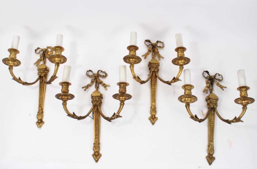Lot 308 - Set of four brass two branch wall lights with ribbon and lion mask decoration