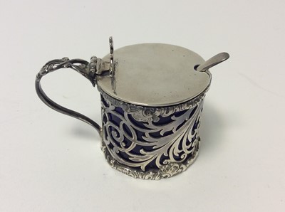 Lot 221 - Edwardian silver mustard pot of drum form with pierced decoration and blue glass liner, hinged cover with raised thumb piece and loop handle, (London 1901)
