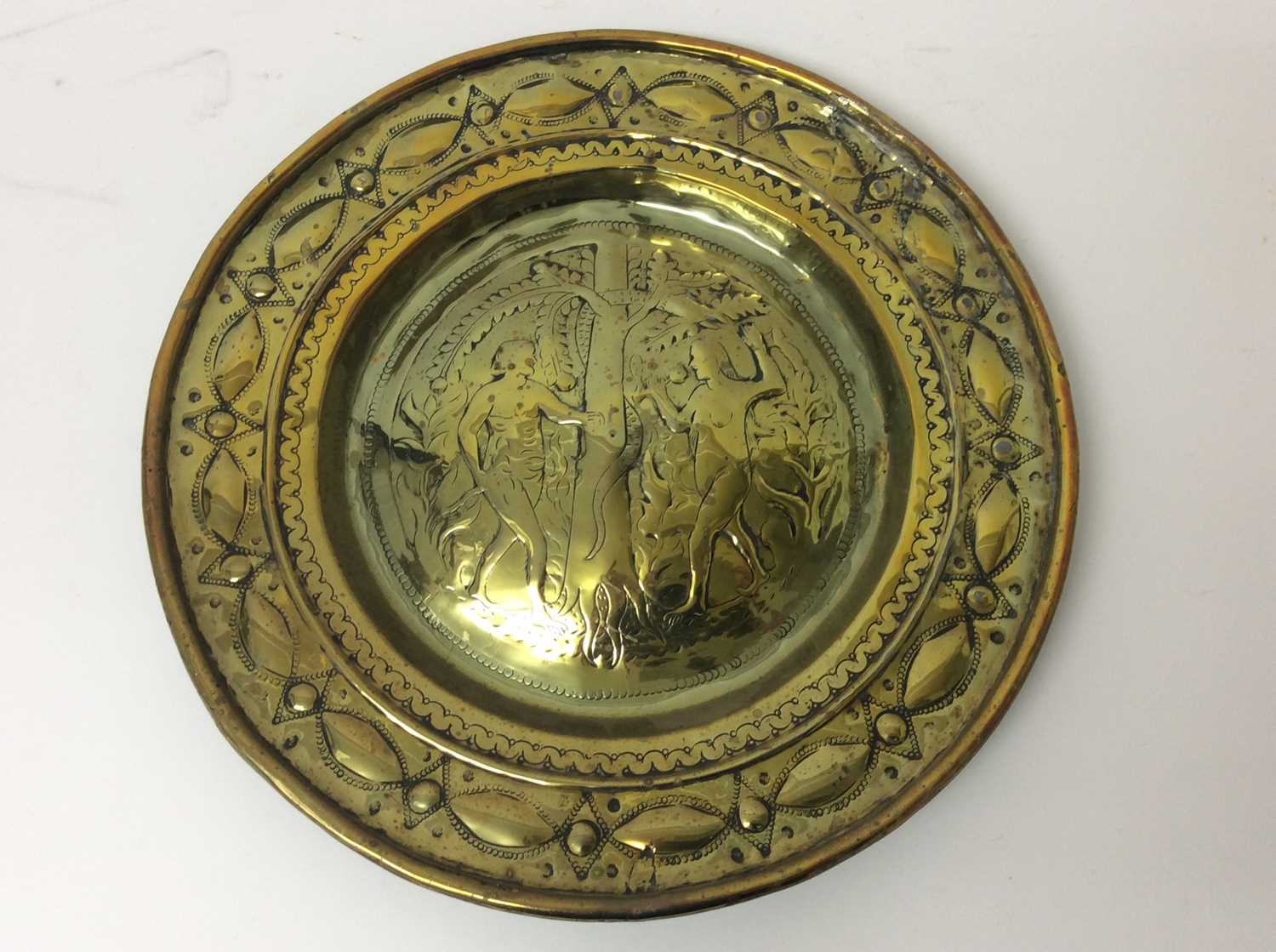 Lot 443 - 17th century German brass alms dish, with Adam and Eve embossed convex roundel and broad geometric border, 35cm diameter 
Provenance: Estate of the Late Jane Sumner