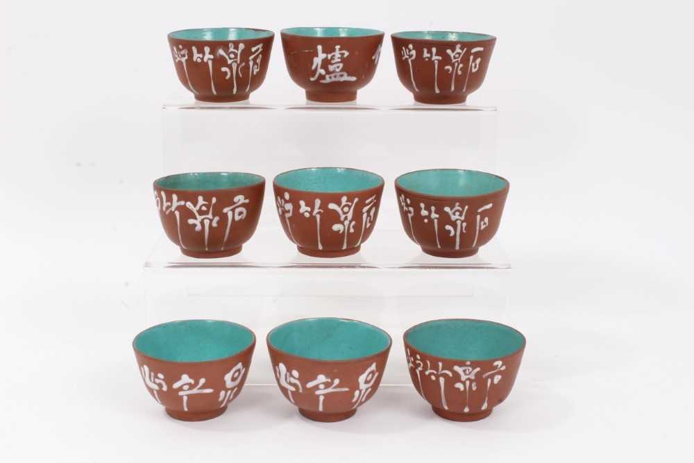 Lot 61 - Set of nine Chinese Yixing pottery tea bowls, painted with calligraphy, enamelled blue inside and on the bases, each approximately 7cm diameter x 4.5cm height