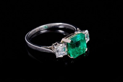Lot 254 - Art Deco style emerald and diamond three stone ring with a central octagonal step cut emerald weighing 2.02cts flanked by two square step cut diamonds estimated to weigh approximately 0.89cts in to...