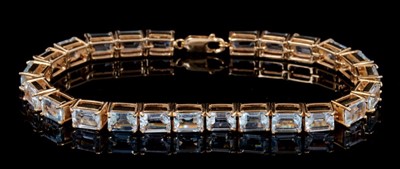 Lot 249 - Aquamarine and gold line bracelet with a continuous row of 24 rectangular step cut aquamarines measuring approximately 7mmx 5mm,,in 9ct gold four-claw setting, length approximately 20cm.