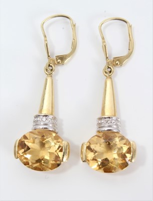 Lot 304 - Pair of citrine and diamond pendant earrings, each with an oval mixed cut citrine and single diamond in 14ct gold setting. 42mm length.