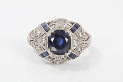 Lot 283 - Art Deco American synthetic sapphire and diamond ring with a central oval mixed cut synthetic blue sapphire flanked by calibre cut sapphires and pierced millegrain scrolls set with old cut diamonds...