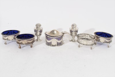 Lot 283 - Edwardian silver mustard pot of oval form with pierced decoration, feather edge, domed hinged cover and blue glass liner, together with a pair of matching silver pepperettes and four matching silve...