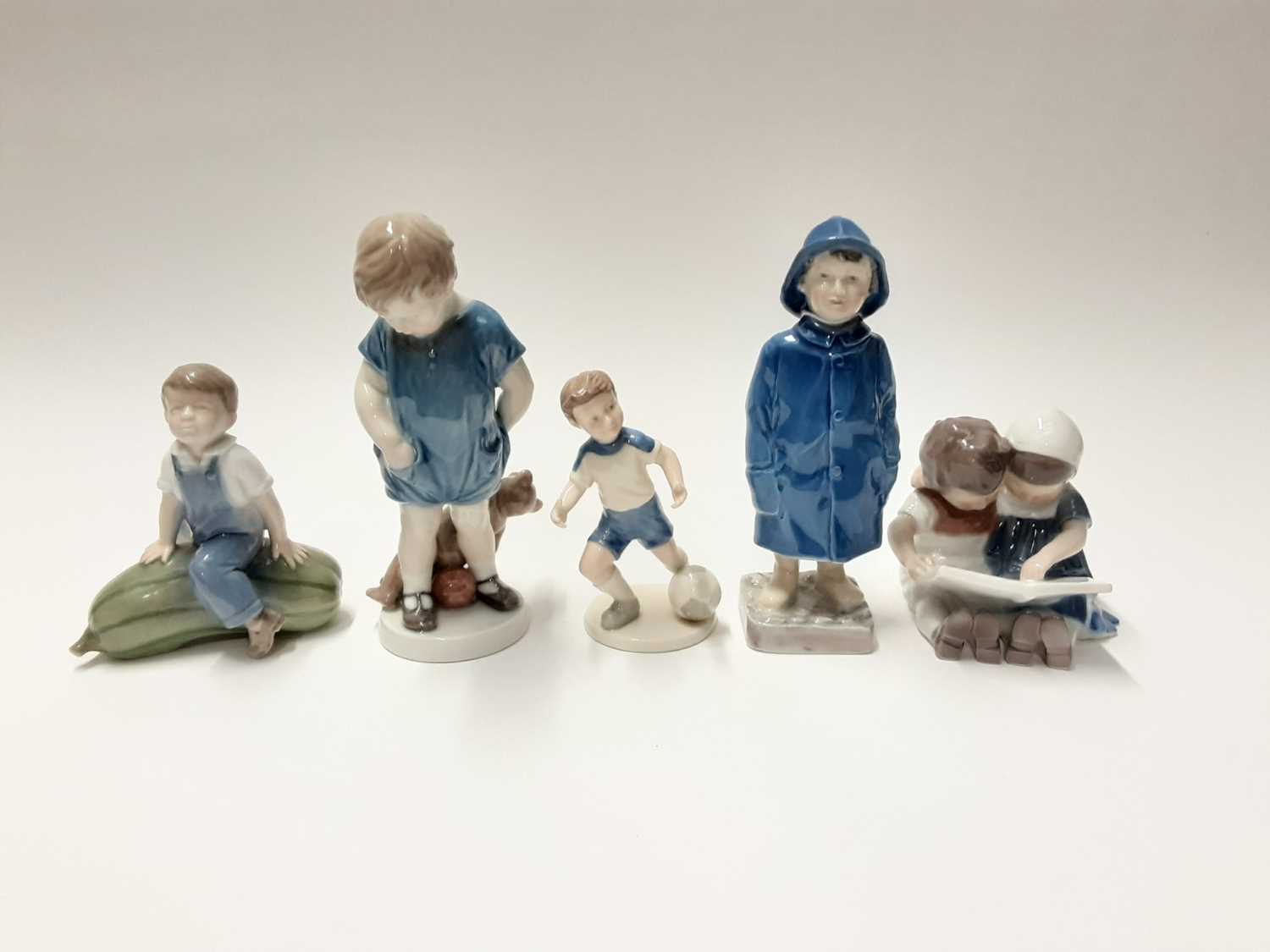 Lot 149 - Five Royal Copenhagen porcelain figures including child in raincoat, boy and girl reading and boy with football