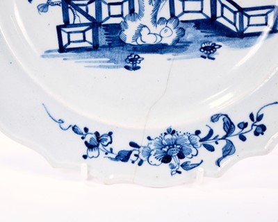Lot 7 - Lowestoft plate, with thickened and shaped rim, painted in blue with flowers and rockwork within a fenced garden, sprigs in the border, 22.2cm diameter