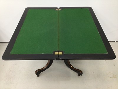 Lot 62 - Victorian ebonised and amboyna inlaid card table, with inlaid fold over rounded rectangular top, well below, raised on four columns with gilt fluted ornament and spread supports on castors, united...