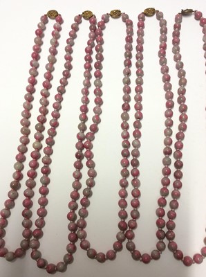 Lot 341 - Collection of twelve Chinese pink hard stone necklaces with round polished beads and oval silver gilt clasps with wire work floral decoration