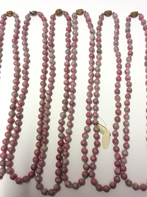 Lot 341 - Collection of twelve Chinese pink hard stone necklaces with round polished beads and oval silver gilt clasps with wire work floral decoration