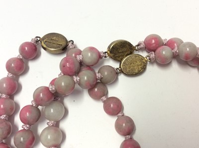 Lot 535 - Collection of twelve Chinese pink hard stone necklaces with round polished beads and oval silver gilt clasps with wire work floral decoration