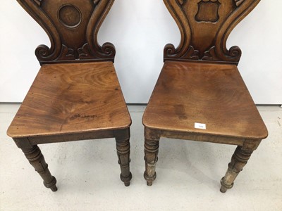 Lot 100 - Pair of Regency mahogany hall chairs with scroll backs, one with circular vacant cartouche, the other with shield shape cartouche, both with solid seats on turned legs with inverted tulip head desi...