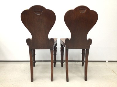 Lot 100 - Pair of Regency mahogany hall chairs with scroll backs, one with circular vacant cartouche, the other with shield shape cartouche, both with solid seats on turned legs with inverted tulip head desi...