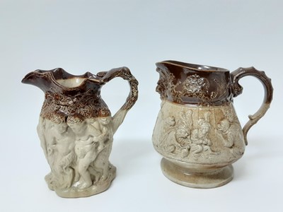 Lot 118 - Two large 19th century relief-moulded salt glazed pottery jugs, the first decorated with Bacchanalian scenes, 22cm high, the second with card-playing monkeys and a mask-form spout, 23cm high