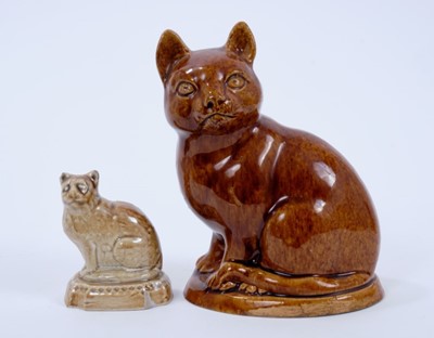 Lot 123 - Mid 19th century treacle glazed pottery model of a cat, shown seated on an oval base, 15cm high, and a smaller lead-glazed model of a cat of similar age, 7cm high (2)