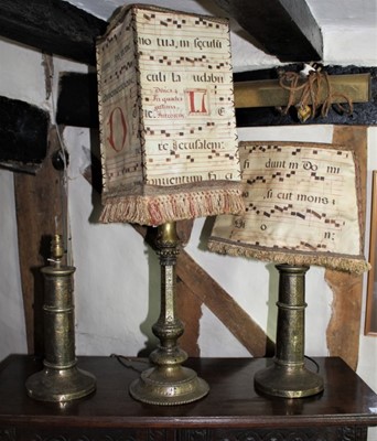 Lot 1543 - Pair of antique brass lamp bases, with tooled arabesque or ornament, bases 36cm high, together with a similar brass lamp, two fitted with clever vellum shades comprised of antique music scores