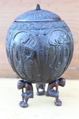 Lot 1763 - 19th century Indian carved coconut cup and cover, the lid decorated with peacock, carved to all sides with figural panels, raised on three figural supports, 19cm high