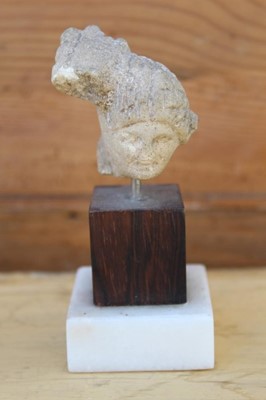 Lot 1767 - Ancient Greek terracotta head fragment, 6cm high, raised on a hardwood and marble stand, together with a similar fragment and one other (3)